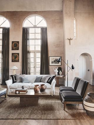 A living room with tall ceilings and arched windows, raw plaster walls and a woven rug