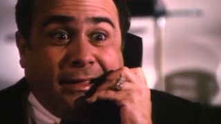 A close up of Danny DeVito speaking on a telephone.