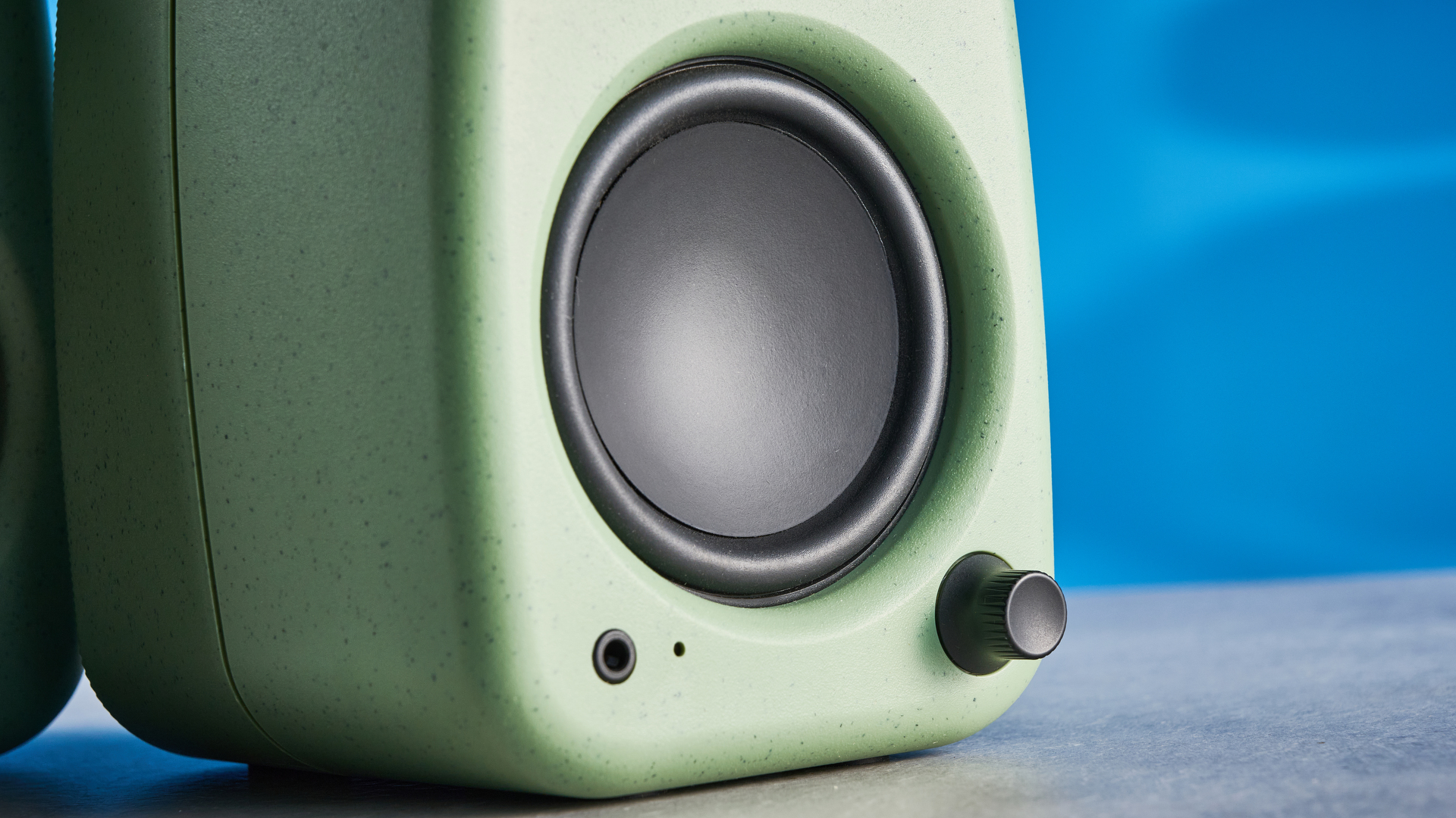 Kanto UKI bookshelf speakers in sage photographed in front of a blue background