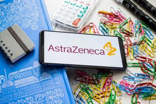 AstraZeneca logo on smartphone surrounded by multi-colored paperclips, notepads, calculator and pens