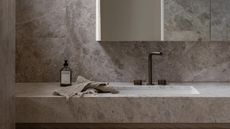A bathroom with a stone countertop and backsplash as well as a sink with dark brass hardware and a mirror above the sink