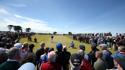 A golfer tees off with spectators surrounding them