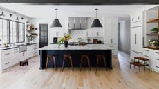 A white kitchen with a dark blue island topped with a marble countertop, with perimeter cabinets topped with granite countertops