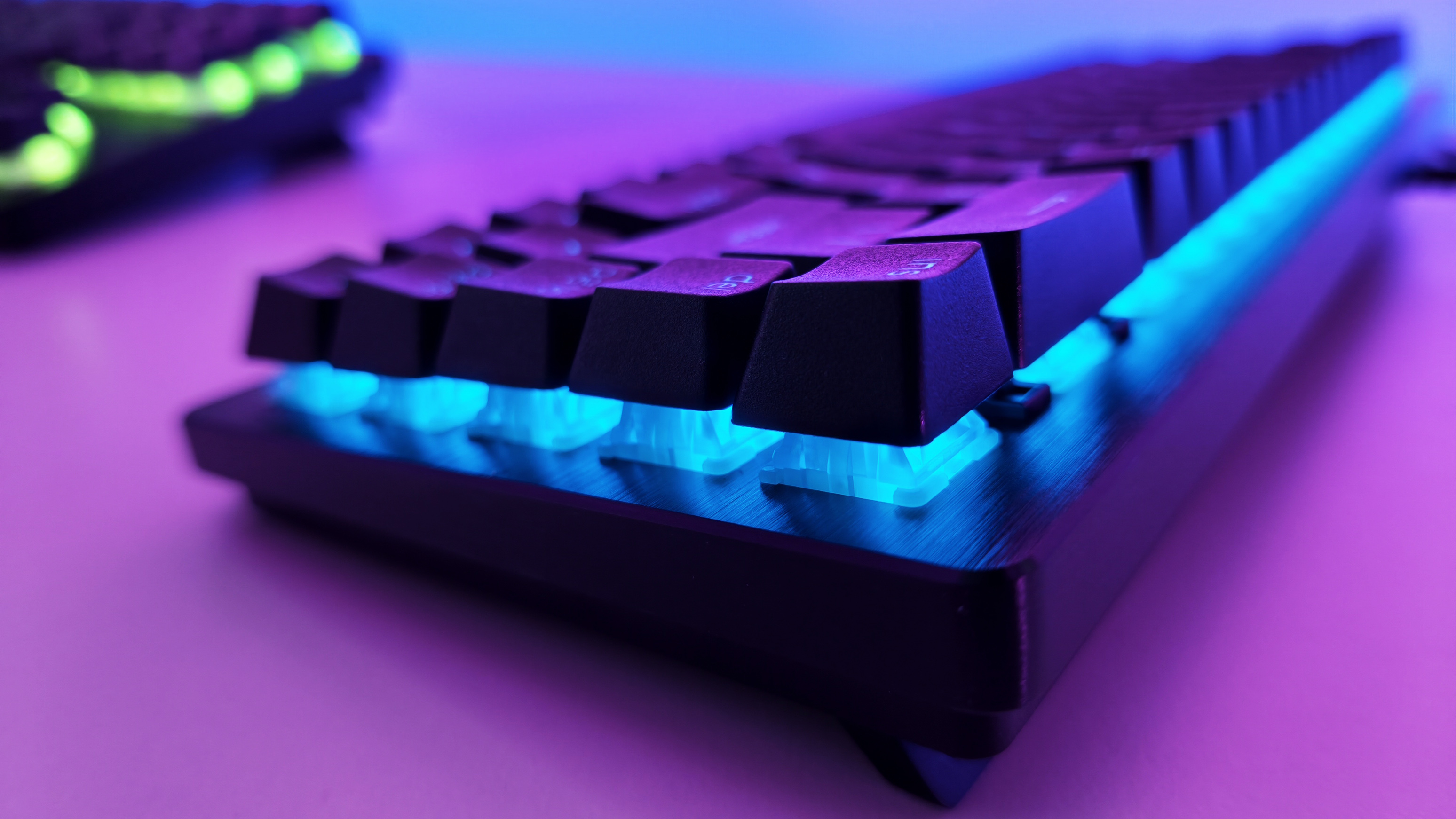 Low-angle close-up of a black Razer gaming keyboard with vibrant cyan RGB backlighting glowing under the keycaps.