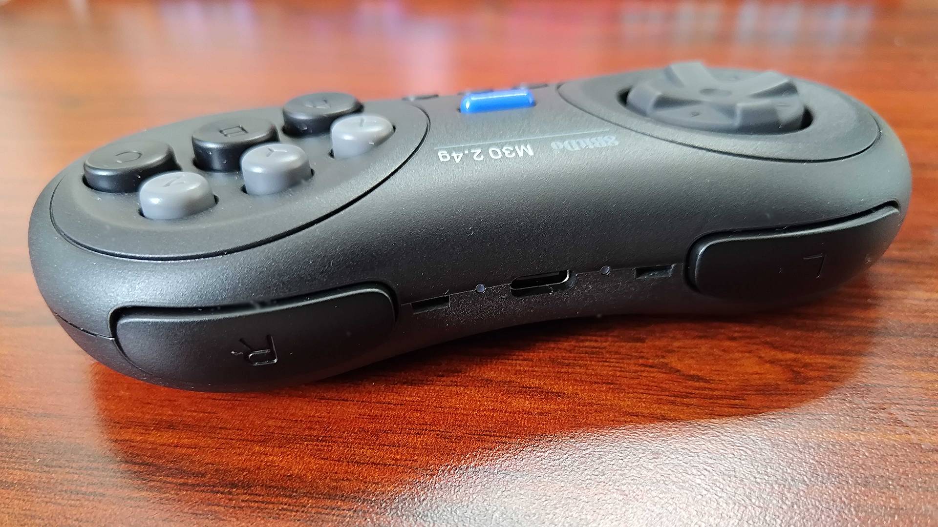 Top view of 8Bitdo M30 Sega Mega Drive/Genesis 23.4Ghz Wireless controller at an angle on woodgrain desk with shoulder buttons and USB-C connector in view.