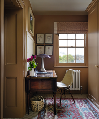 office corner with brown painted walls with desk and chair and rug infront of window