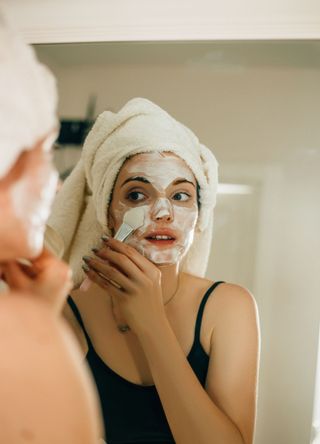 Side view shot of young woman applying facial cosmetic mask in bathroom.