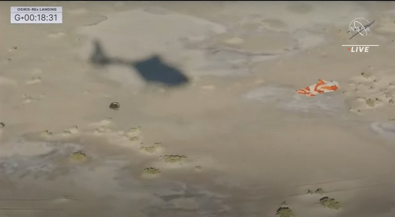 Shadow of helicopter is seen with the parachute and sample capsule on the ground.
