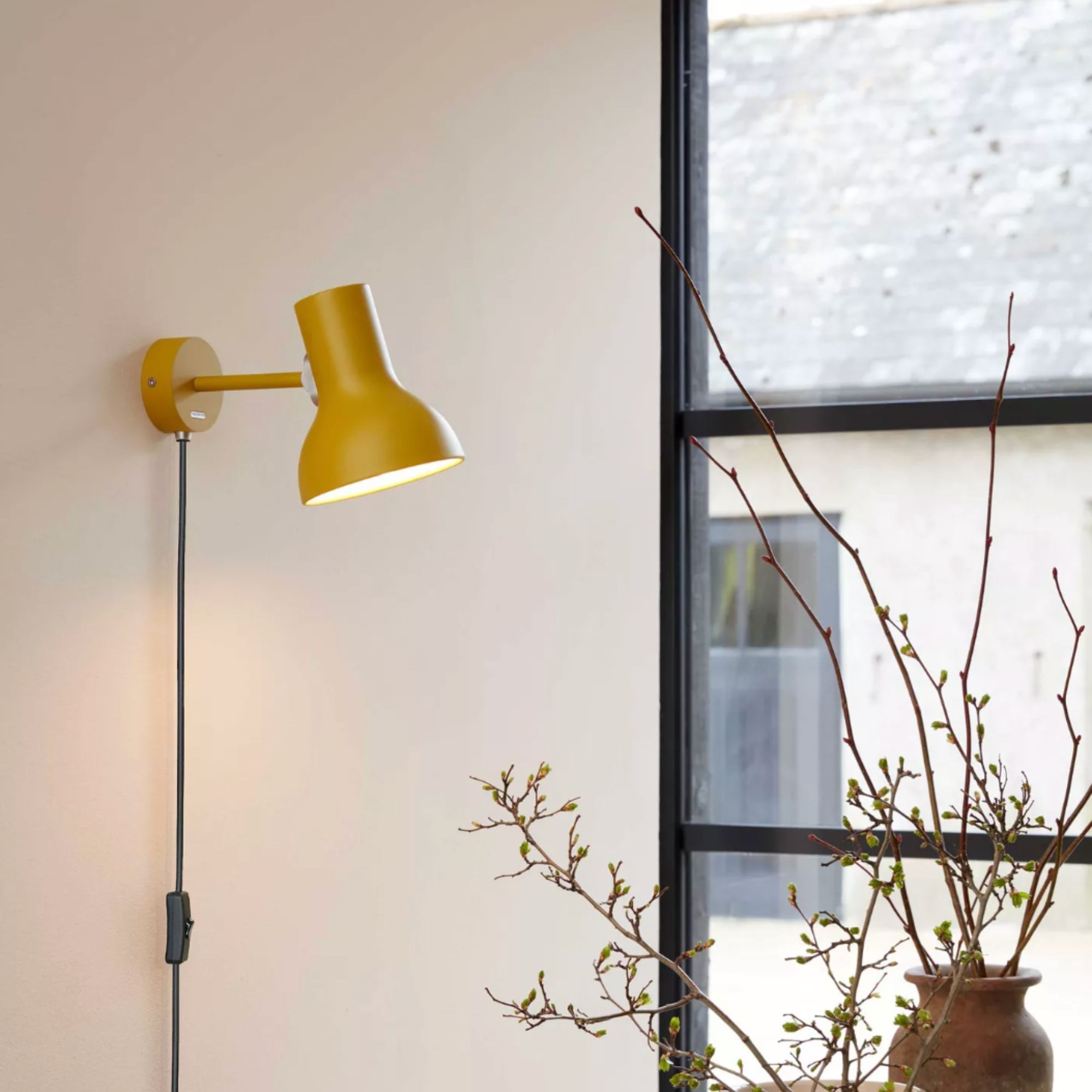 AnglepoiseType 75 Mini Margaret Howell Edition Plug-In Wall Light, Yellow Ochre, hanging on wall beside window with plant