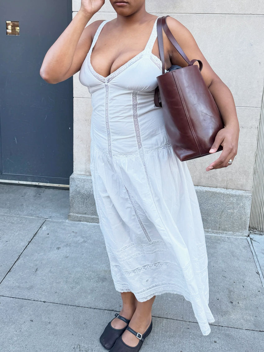a woman wearing a white dress, brown leather shoulder bag, and Mary Jane black flats