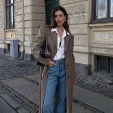 Woman wears white shirt, blue jeans and brown overcoat