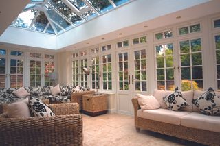a simple white orangery with a glass roof and French doors, and rattan furniture with black, white and pink cushions