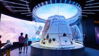 a white space capsule on display in a museum, with several people nearby