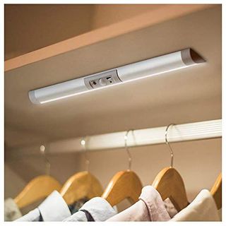 Automatic Motion Sensor Closet Light stuck underneath a shelf over a hanging rail with wooden hangers and linen shirts