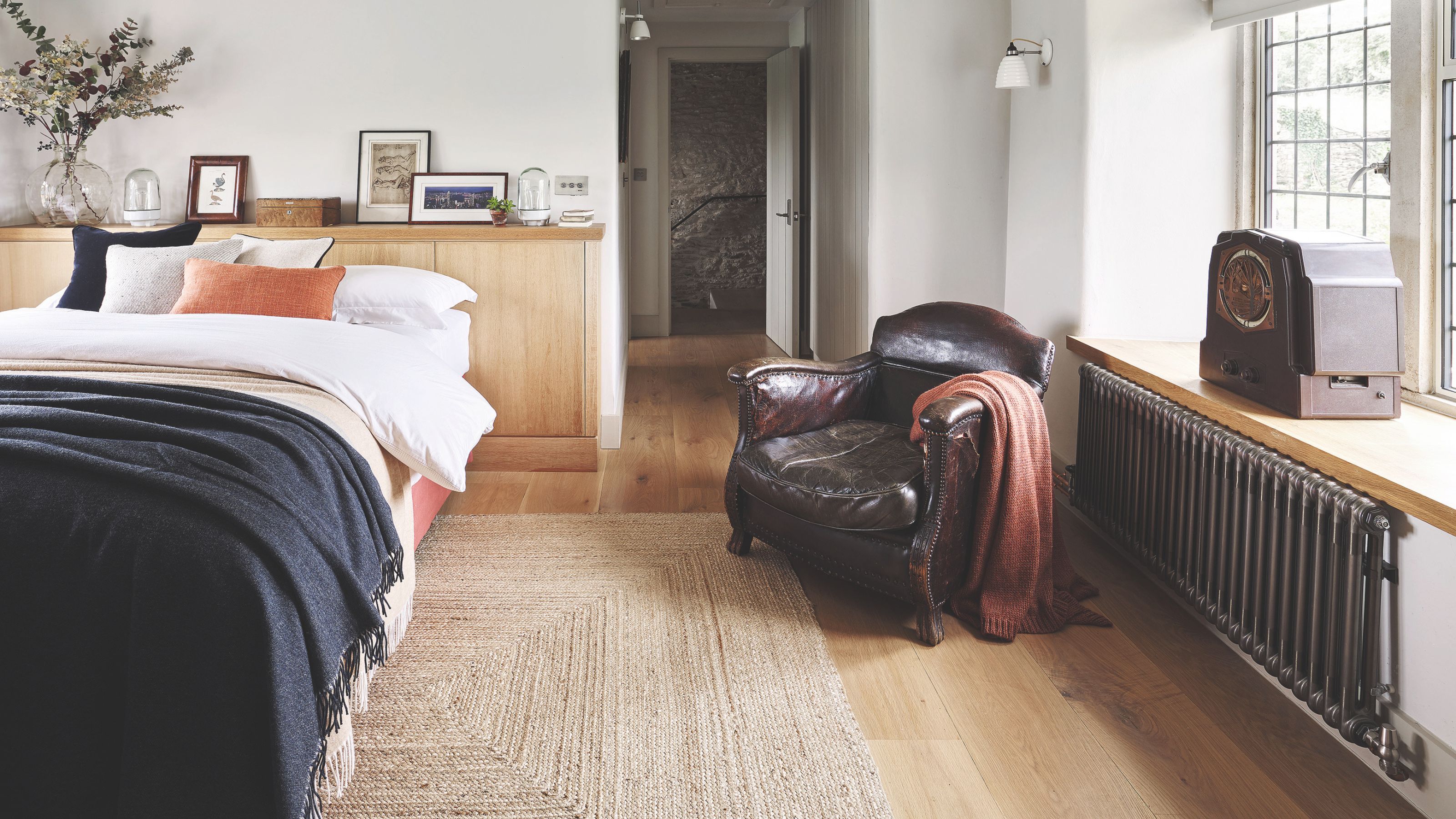Bedroom with wooden flooring and a bed on the left, with an accent chair and a window seat on the right