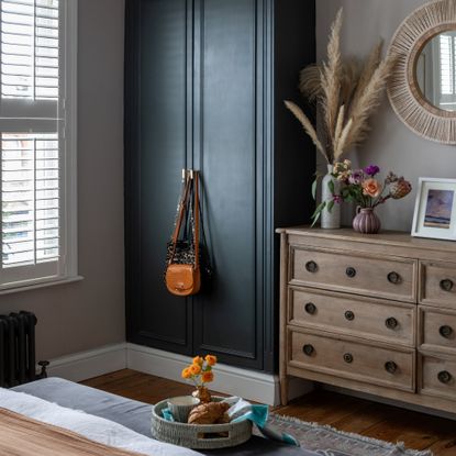 A bedroom with a navy built-in wardrobe and a natural set of drawers