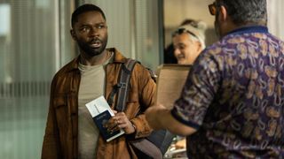 David Oyelowo in a brown jacket as Dave holds a passport and looks surprised in Role Play.