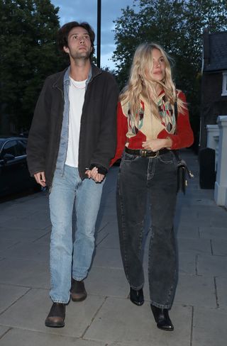 Sienna Miller wears a red cardigan and black jeans.