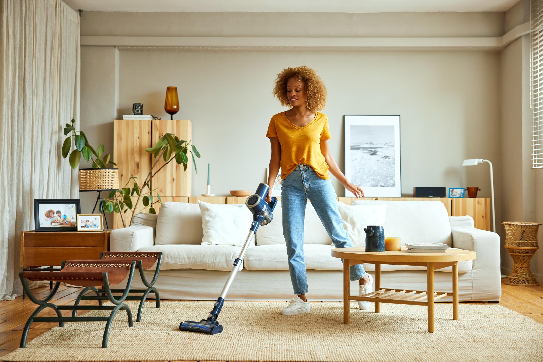  A woman cleaning a beige rug with a hoover in her home. 
