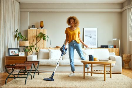 A woman cleaning a beige rug with a hoover in her home.