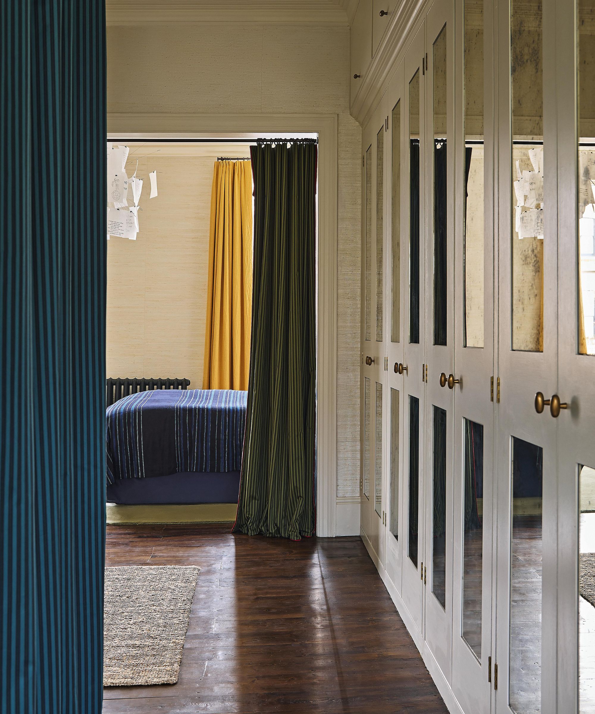 a walk through dressing area in a bedroom in london with mirrored closet doors and blue drapes