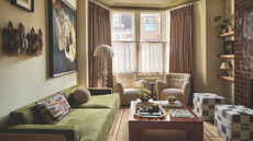 a cozy living room with a green couch, a large coffee table, two white chairs, and a large bay window