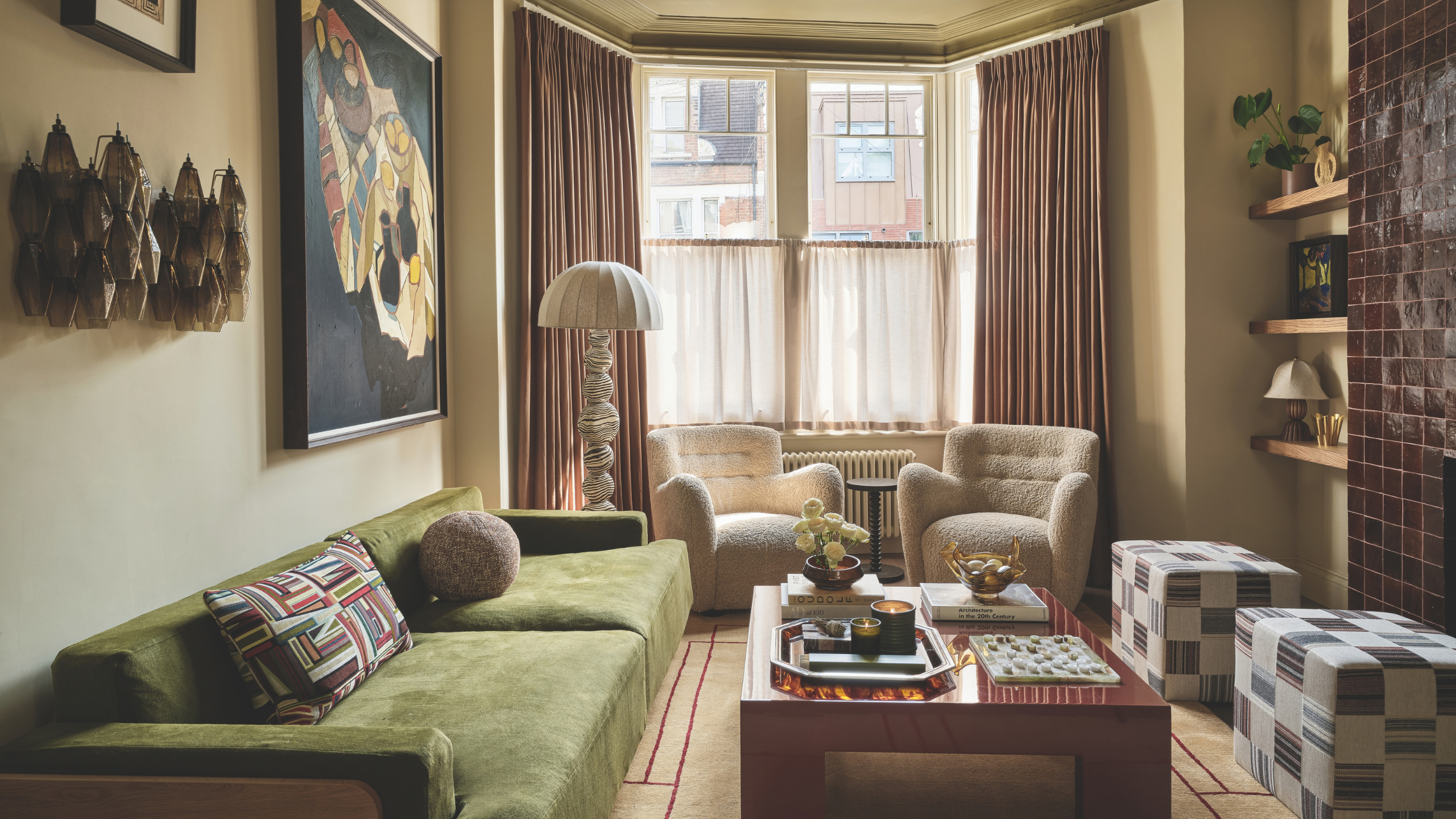 a cozy living room with a green couch, a large coffee table, two white chairs, and a large bay window
