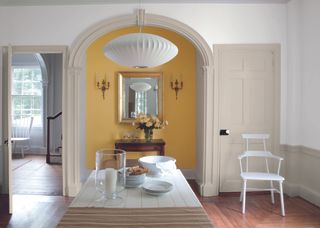 dining room with yellow painted alcove, dining table, wall lights, mirror, pendant, wooden flooring
