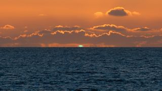 A green flash appears on the horizon during a sunset over the ocean