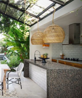An outdoor kitchen under a permanent glass structure with a huge granite work top