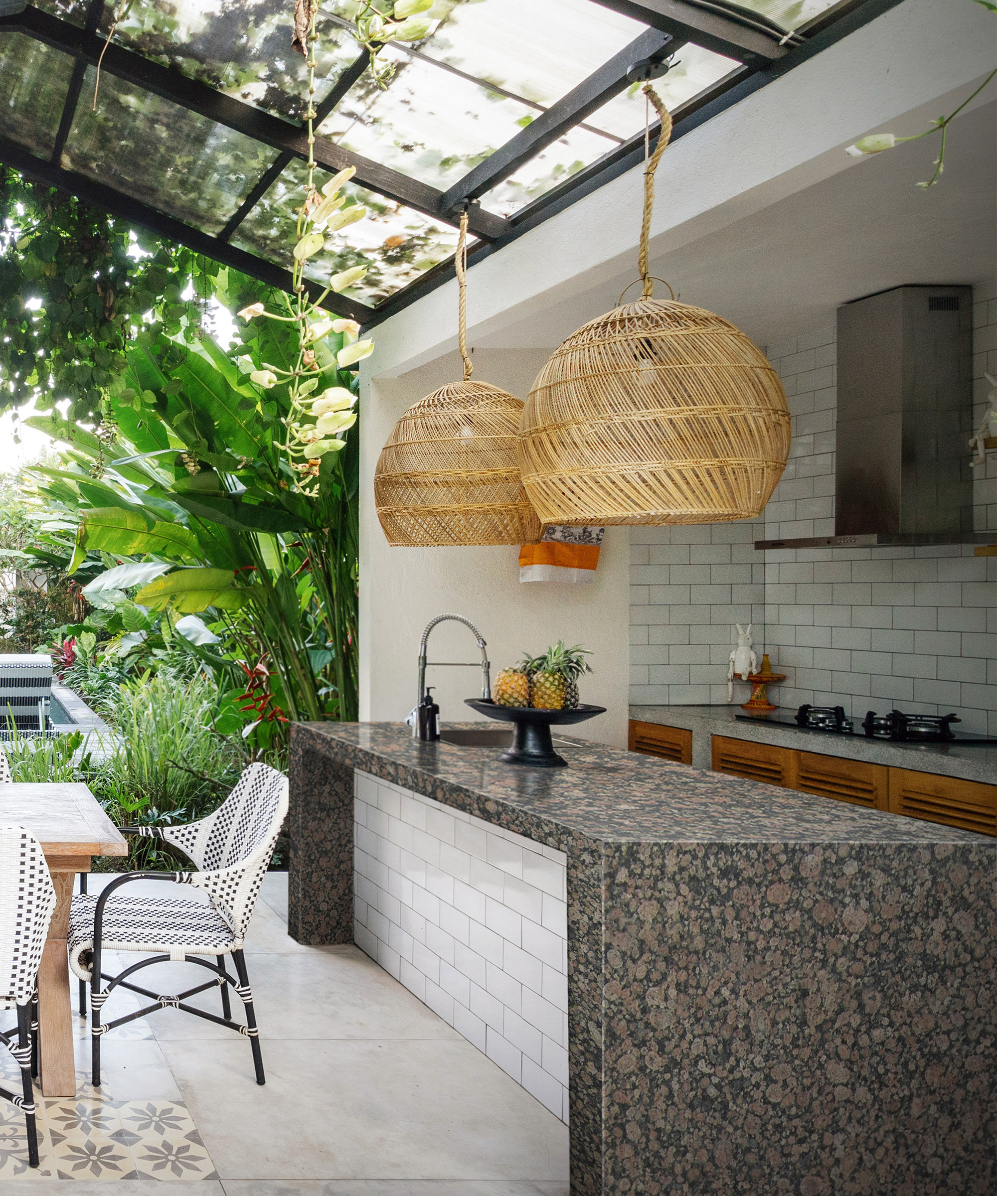 An outdoor kitchen under a permanent glass structure with a huge granite work top