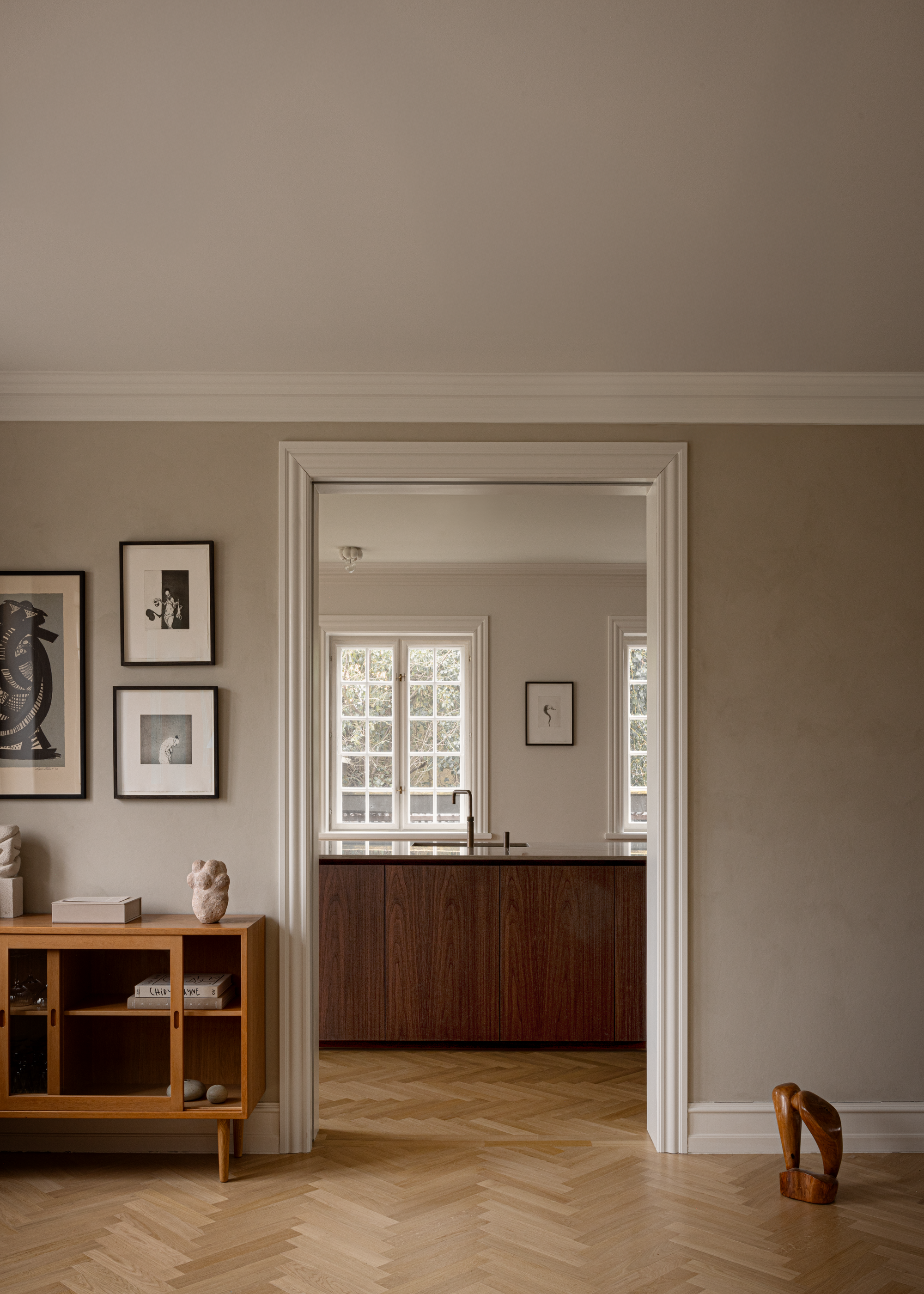 A living space with a side table with decor, and a doorway looking into a minimalist kitchen