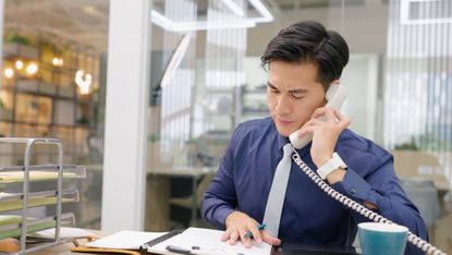 A young man answers the phone in an office.