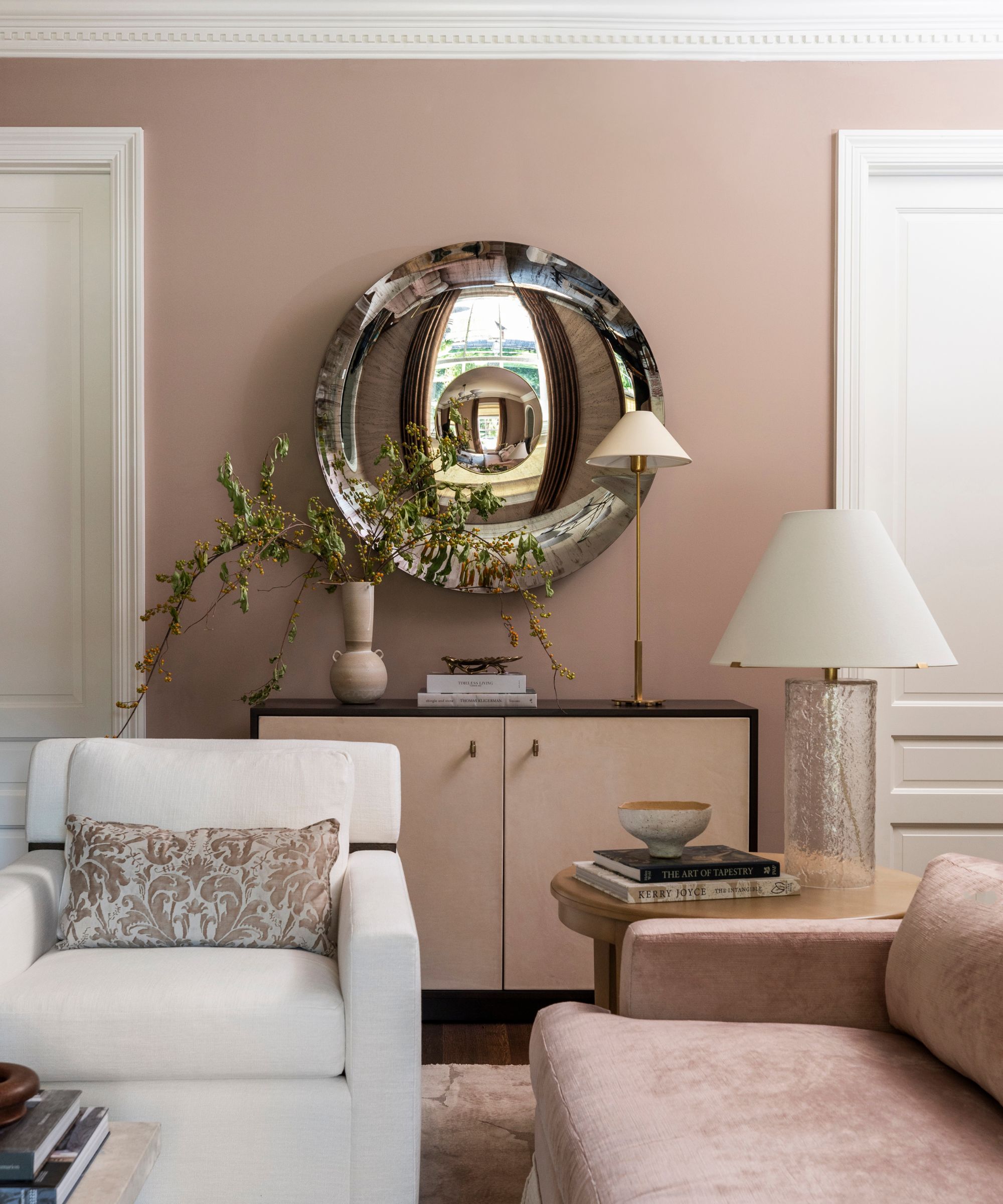 A living room with plaster pink walls, a pink sofa, white ceiling and doors, a cream sofa, and transitional decor.