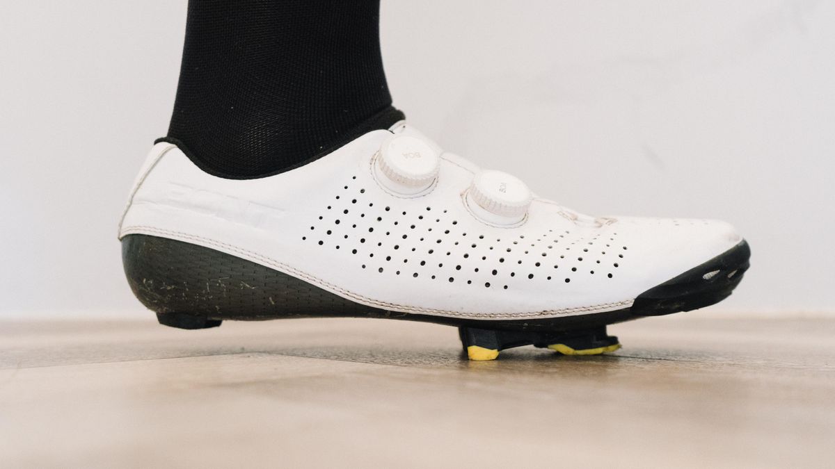 A close up of a white cycling shoe with a black socked foot in it