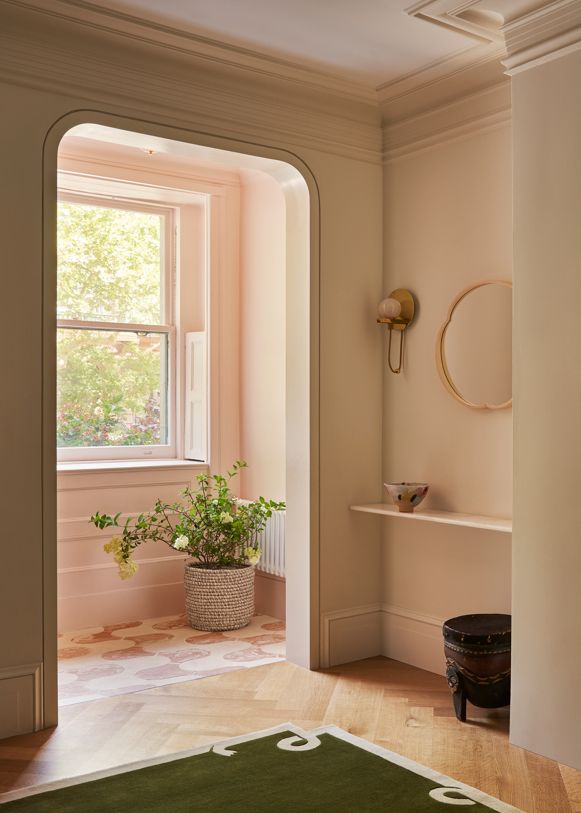 A bright room with a hanging mirror, a wall sconce, a green carpet, a potted plant, and a low stool