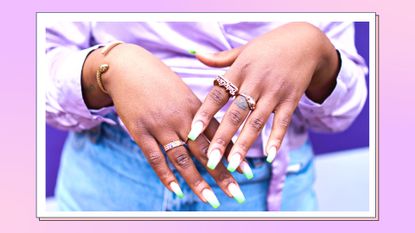 Spring nails 2023: Close up of woman's hands with lots of gold rings and painted grey and white nails/ in a purple and pink template