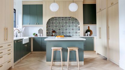Modern kitchen with large green painted wooden island, two stools and tile stove backsplash