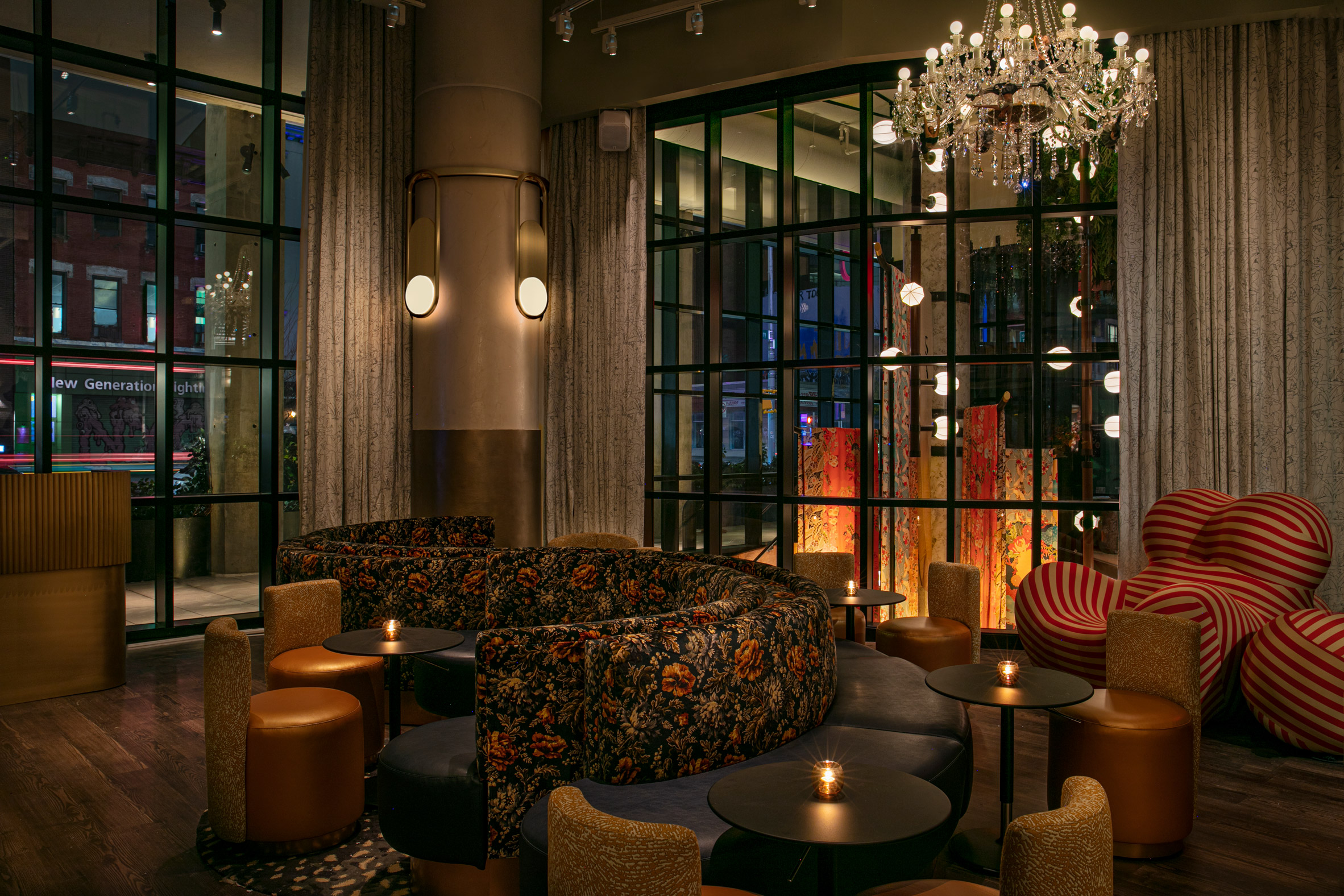 A layeredly decorated hotel features extravagant decor in its communal areas, including sumptuous chandelier, paper lanterns, lush plants, and patterned upholstery, with quirky, contemporary rooms characterized by color-block interiors and textural surfaces.