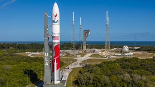 A white, red and gray rocket rolls to an oceanfront launchpad.