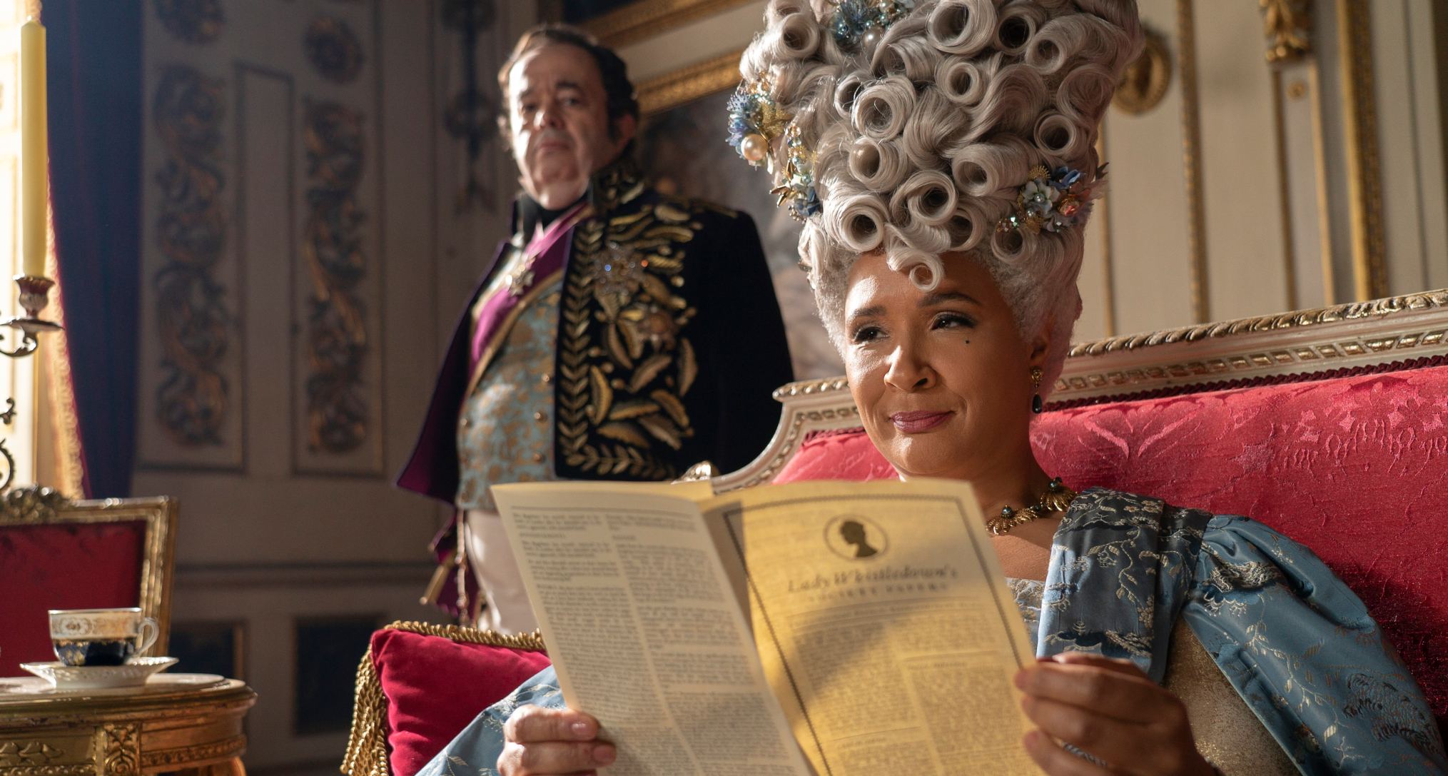 queen charlotte smirking as she reads the society papers on her throne in bridgerton