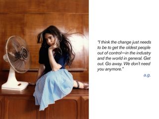 Ariana Greenblatt sitting on table wearing blue top, checkered skirt, and satin ballet flats.