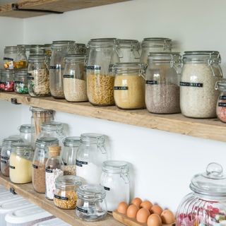 Wooden shelves lined with clear jars storing food, labelled
