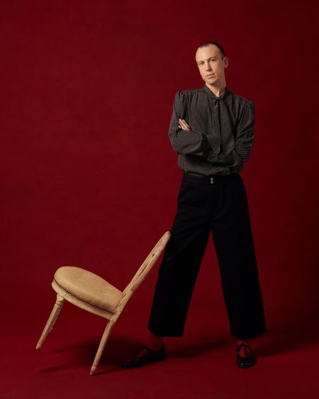 Michael Diaz-Griffith with a chair leaning on his leg, red background