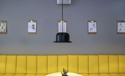 A hanging light with a bowler hat as a lamp shade. Yellow couch running along the wall. 