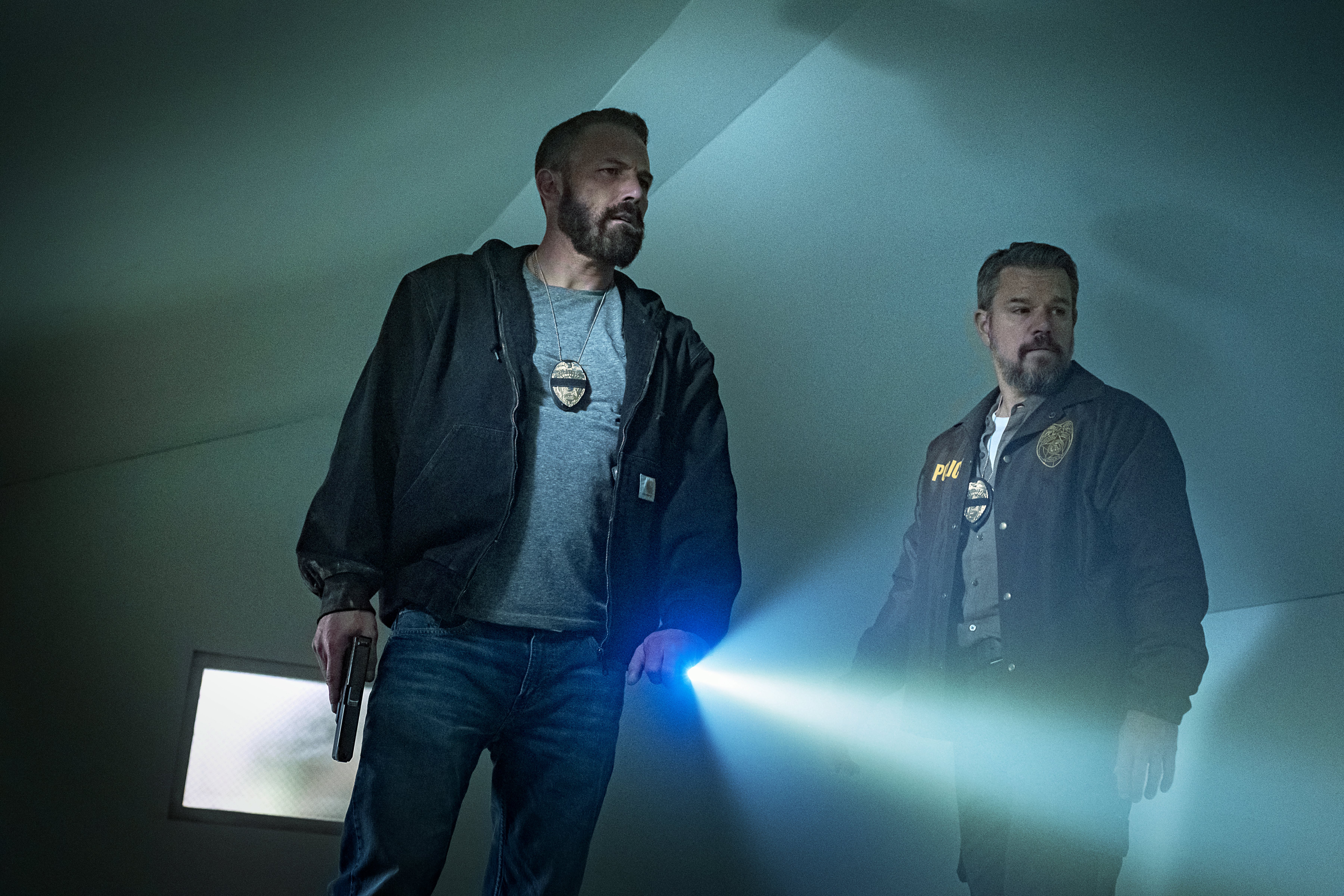 Ben Affleck as Detective Sergeant J.D. Byrne and Matt Damon as Lieutenant Dane Dumars walking through a dark abandoned room with a flashlight in the movie the rip
