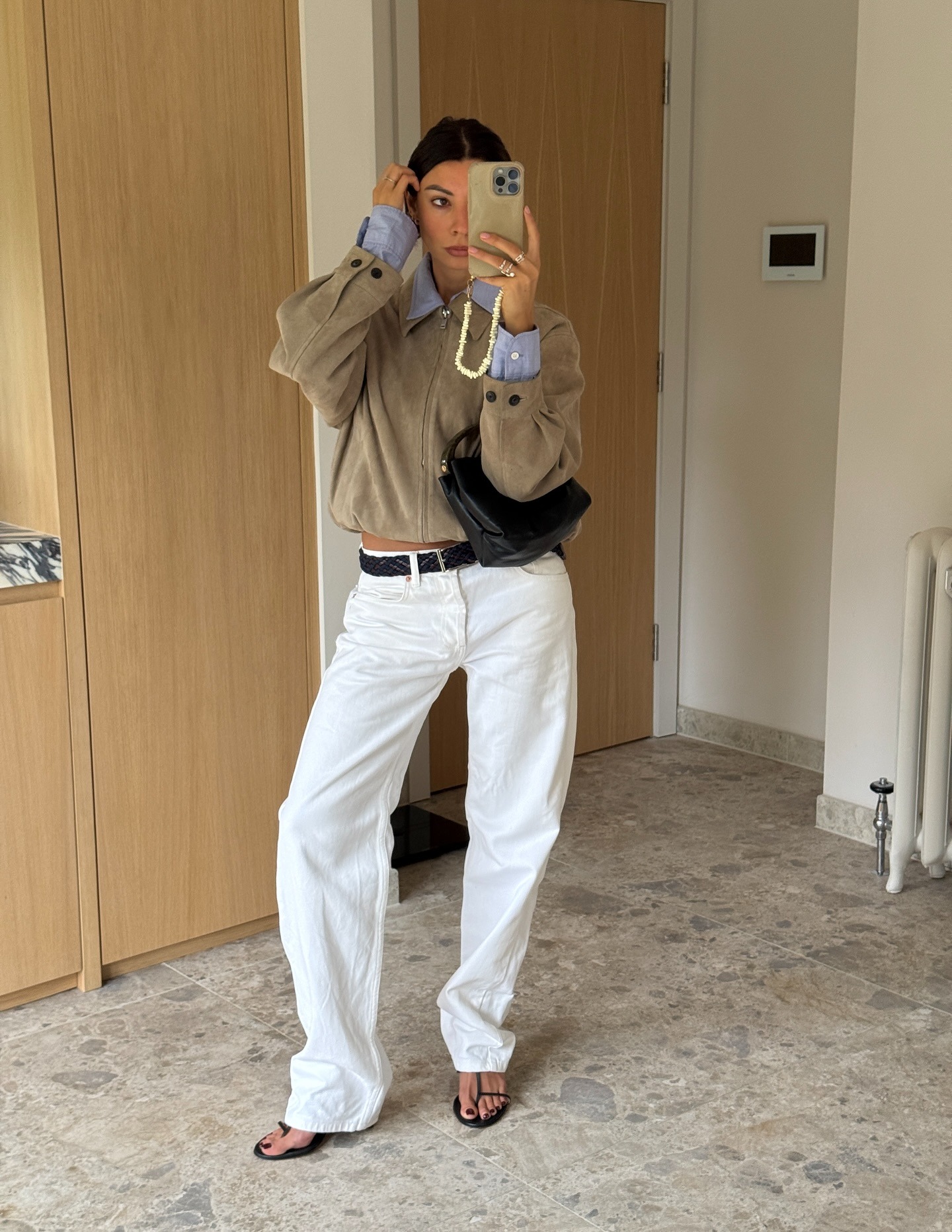 Woman wears suede jacket, blue shirt, white jeans, black sandals