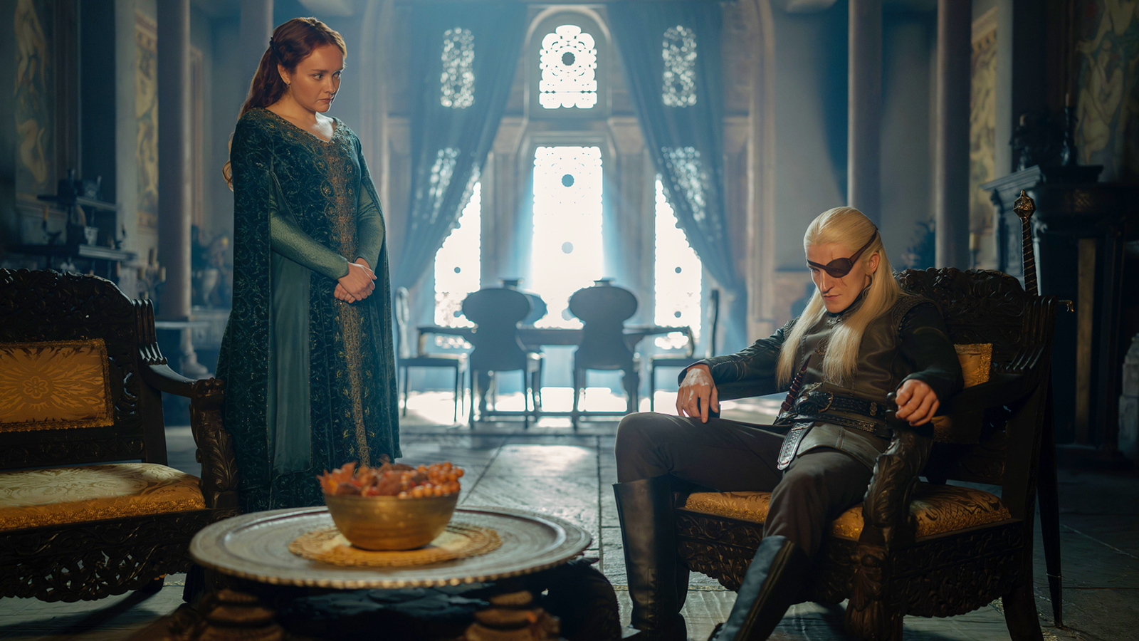 Alicent standing with hands clasped and Aemond sitting in a chair in House of the Dragon season 3