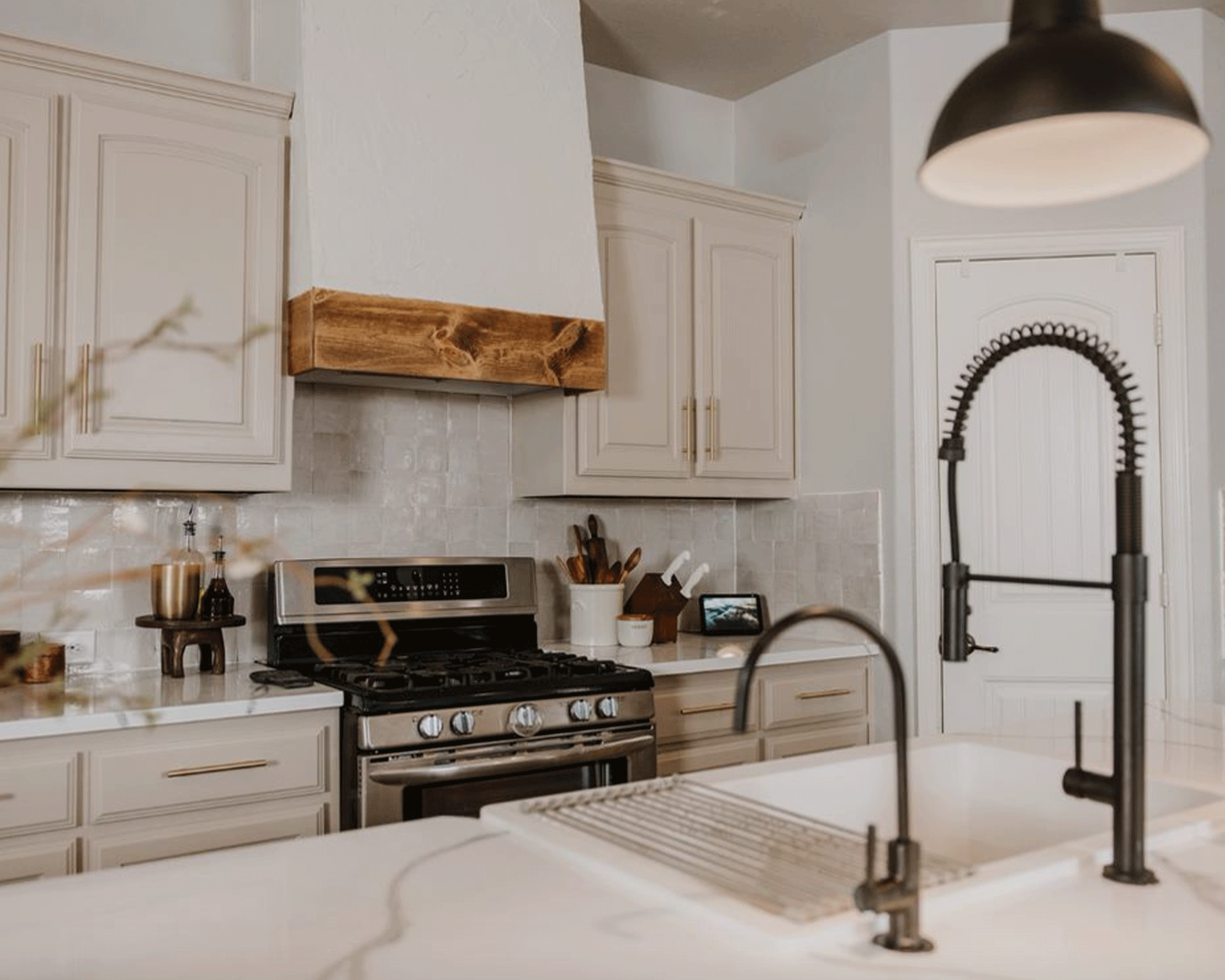 modern kitchen view with large white island with a sink and black taps on it, a stainless steel cooker, and extraction fan with wooden fringe