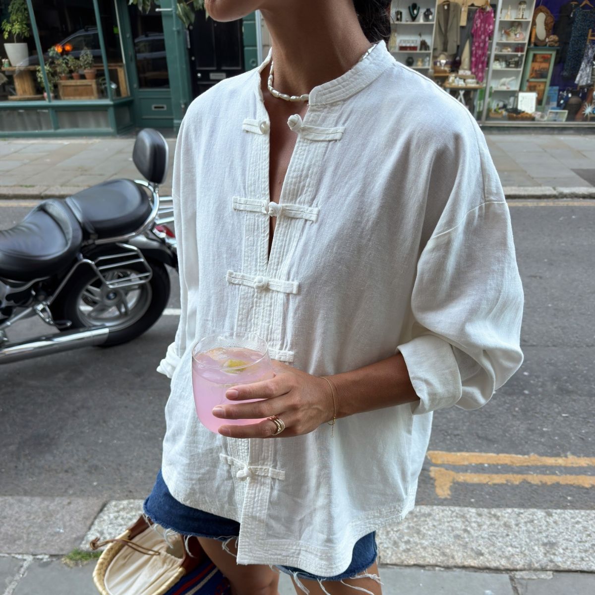 Woman wearing white linen shirt and denim shorts.